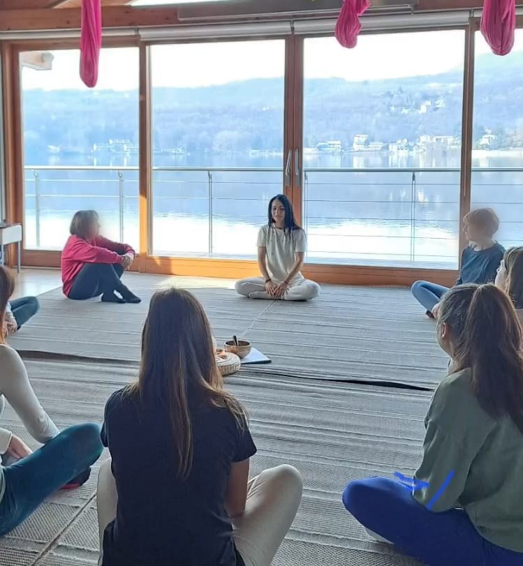 Un gruppo in pratica di respiro e meditazione, seduto in cerchio in una sala affacciata sul lago